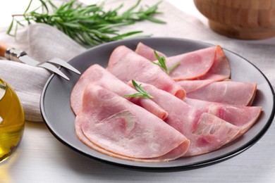 Photo of Tasty ham with rosemary and carving fork on white wooden table, closeup