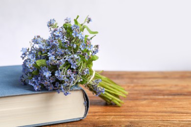 Bouquet of beautiful forget-me-not flowers and book on wooden table against light background, space for text