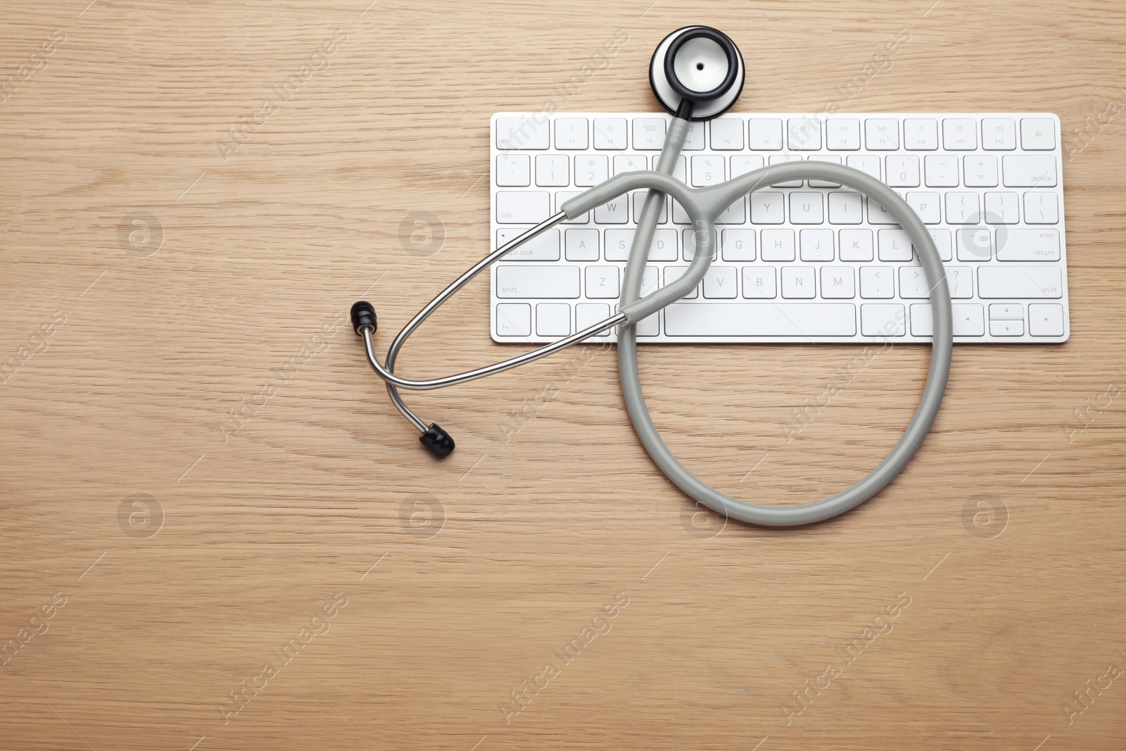 Photo of Computer keyboard with stethoscope on wooden table, top view. Space for text