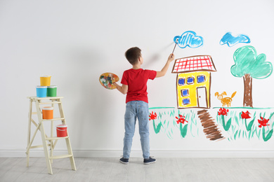 Little child drawing house on white wall indoors