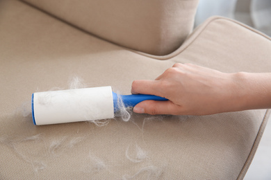 Woman removing hair from beige sofa, closeup