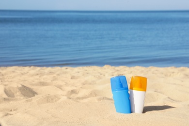 Photo of Bottles of sunblock in beach sand near sea. Space for text