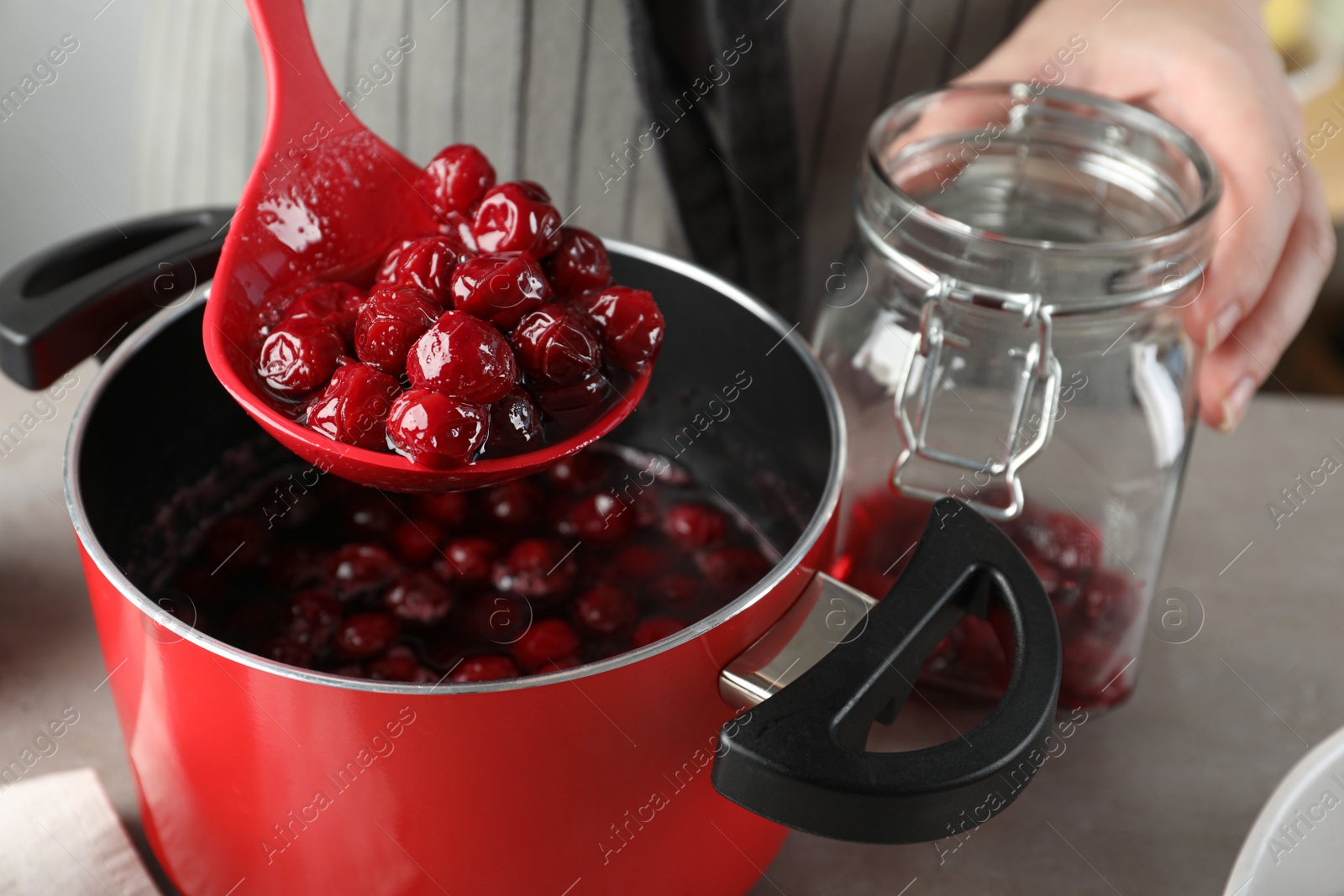 Photo of Woman making pickled cherries at table indoors, closeup