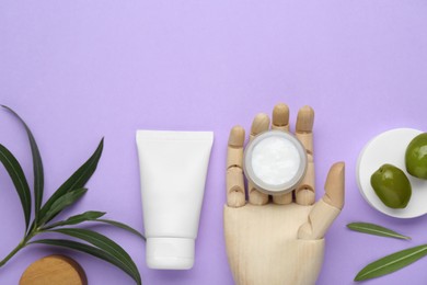 Cosmetic products with olive essential oil and wooden mannequin hand on violet background, flat lay. Space for text