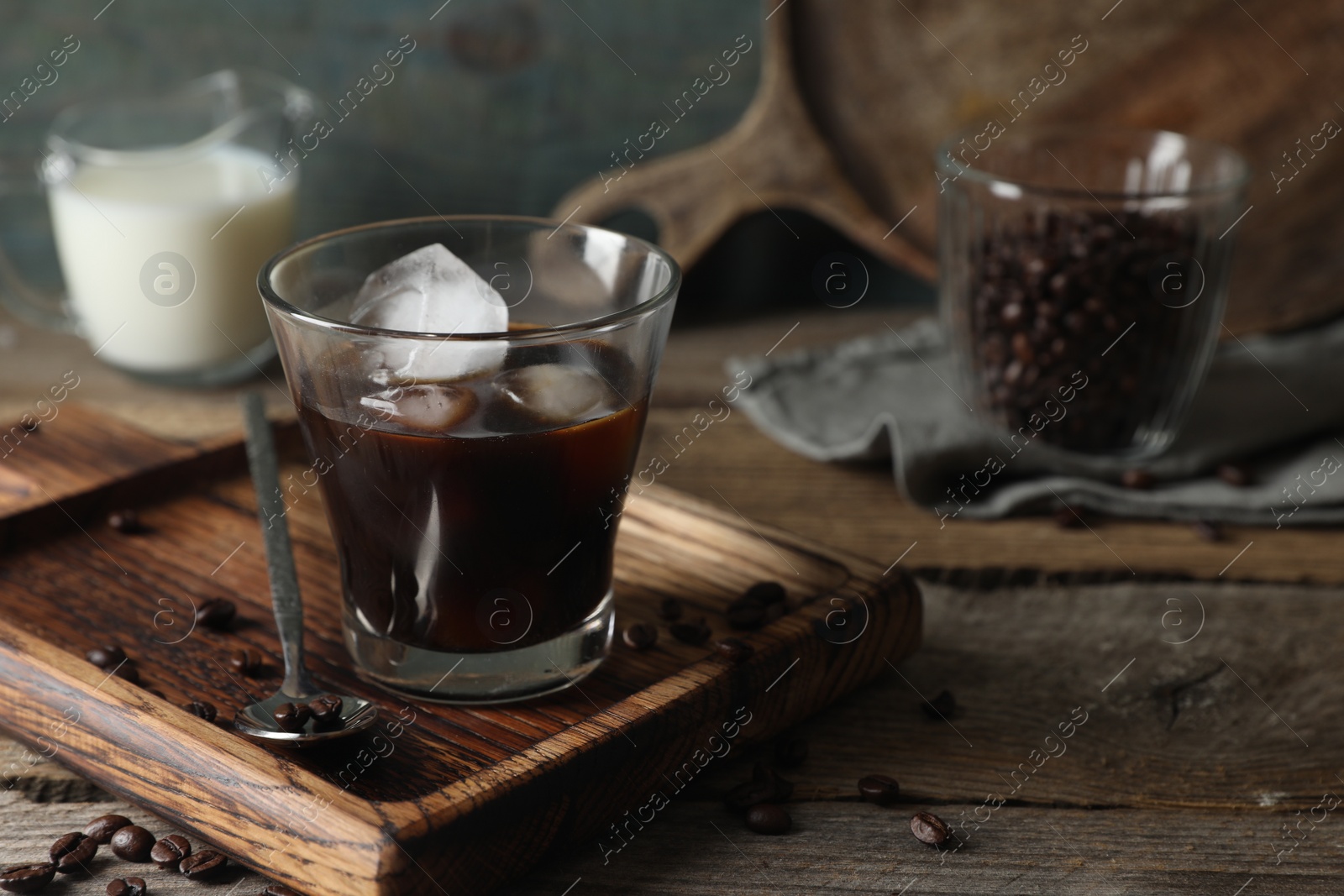 Photo of Glass of delicious iced coffee and beans on wooden table, space for text