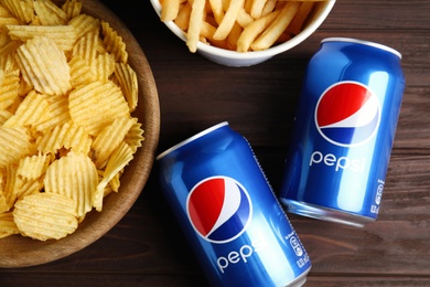 MYKOLAIV, UKRAINE - FEBRUARY 15, 2021: Cans of Pepsi and snacks on wooden table, flat lay