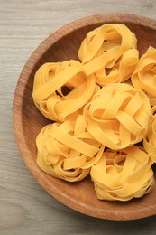 Photo of Raw tagliatelle pasta in bowl on light grey wooden table, top view