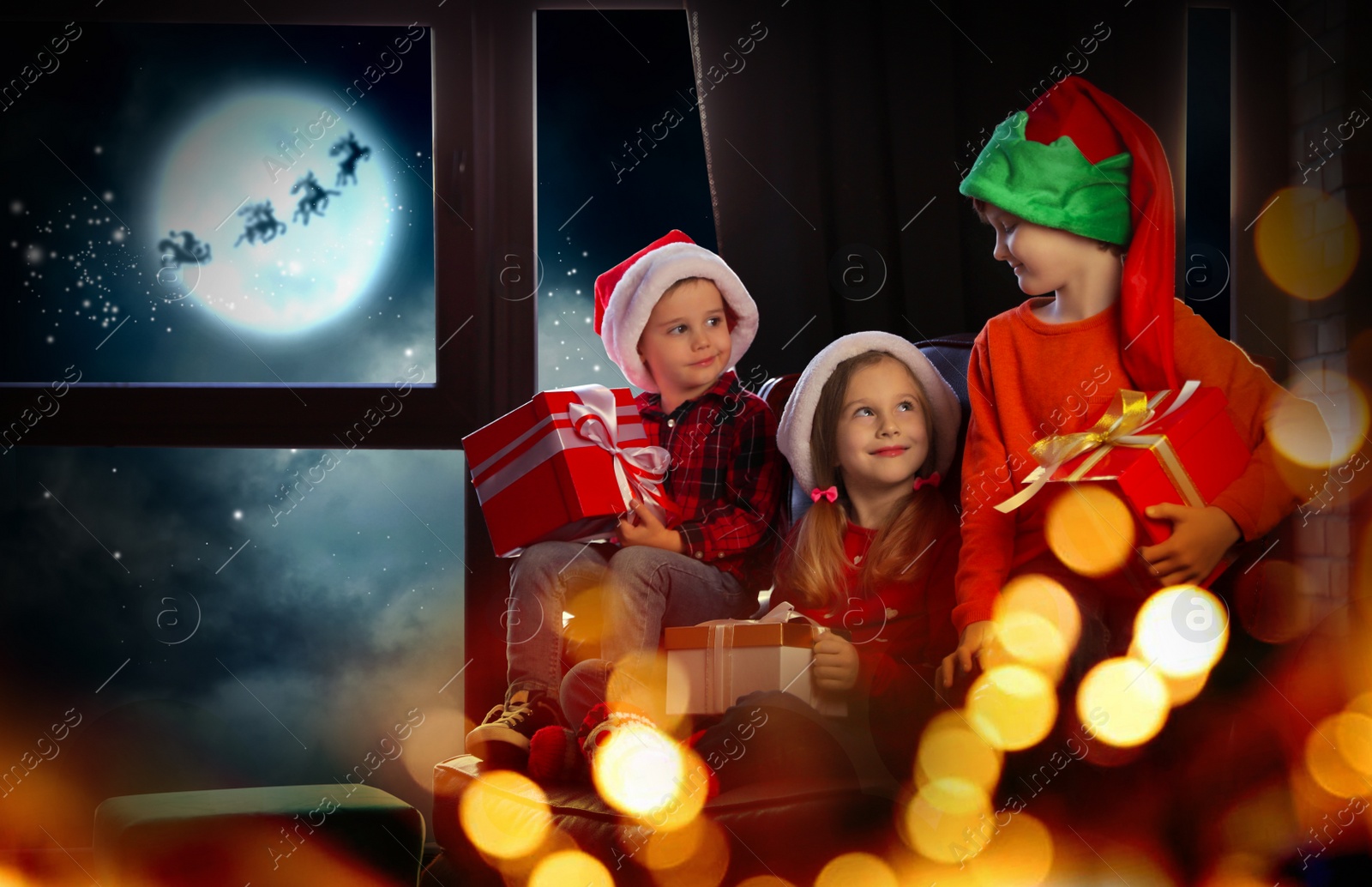 Image of Little children with Christmas gifts near window at home. Presents from Santa Claus
