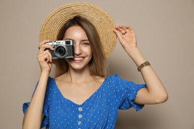 Photo of Beautiful young woman with straw hat and camera on beige background. Stylish headdress