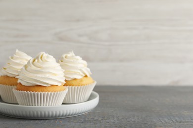 Delicious cupcakes with cream on grey wooden table. Space for text