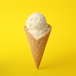 Photo of Delicious ice cream in waffle cone on yellow background