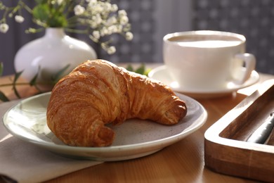 Photo of Tasty croissant served on wooden table indoors, closeup