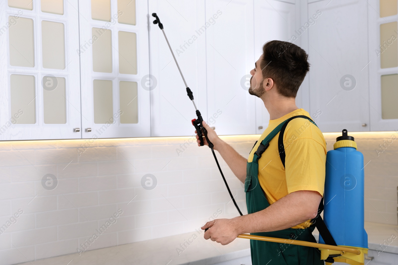 Photo of Pest control worker spraying insecticide on furniture in kitchen