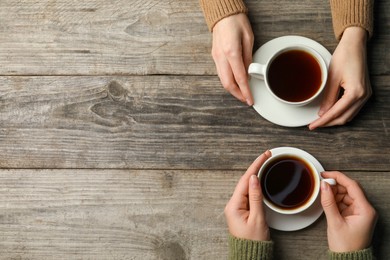 Women with cups of aromatic coffee at wooden table, top view. Space for text