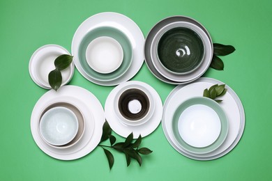 Photo of Different dishware and leaves on green background, flat lay