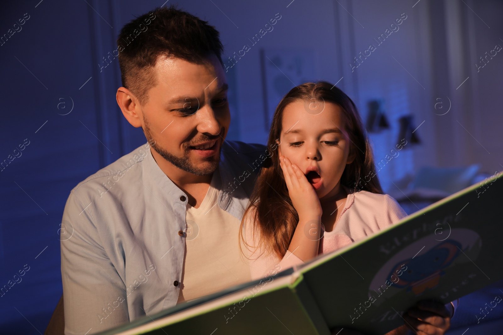 Photo of Father reading bedtime story to his daughter at home