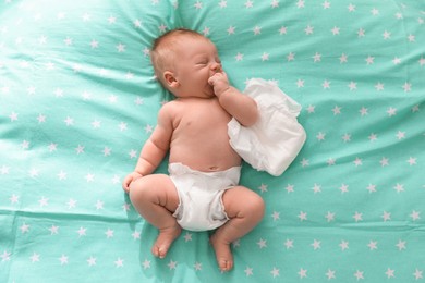 Photo of Cute little baby in diaper lying on bed, top view