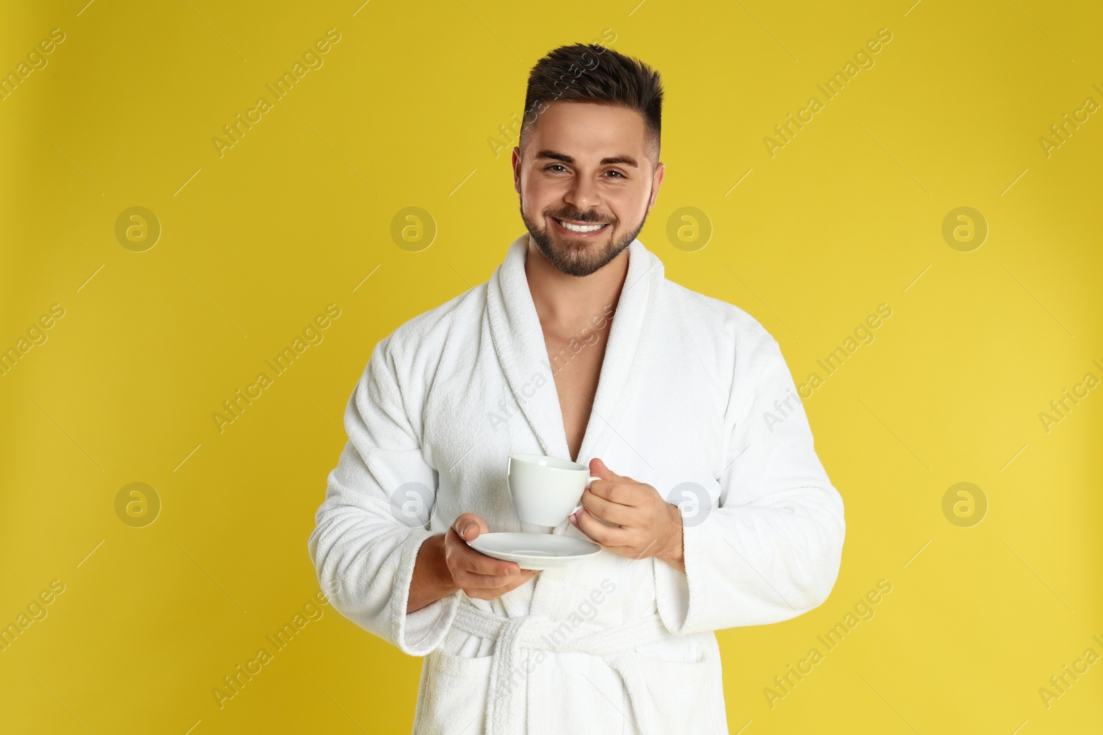 Photo of Young man in bathrobe with cup of coffee on yellow background