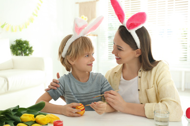 Happy mother and son with bunny ears headbands painting Easter egg at home