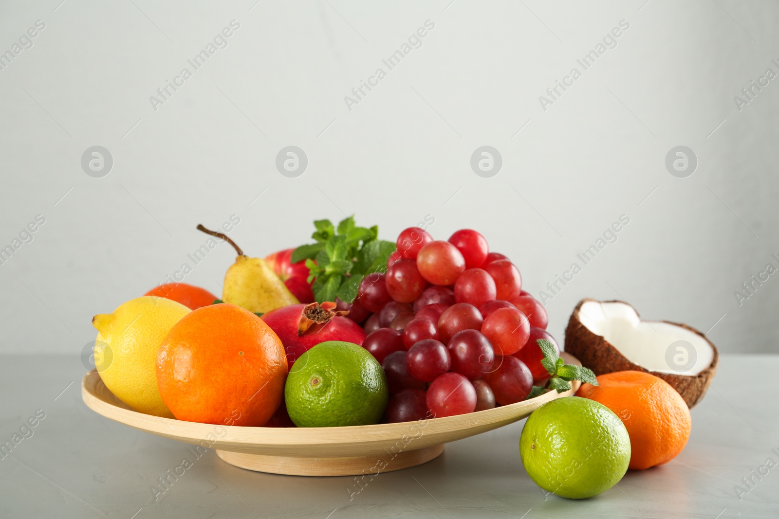Photo of Wooden plate and different ripe fruits on grey table
