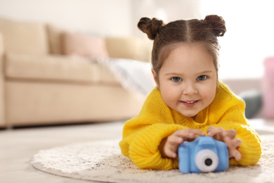 Photo of Little photographer with toy camera on floor at home. Space for text