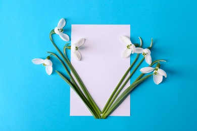 Beautiful snowdrops and card on light blue background, flat lay. Space for text