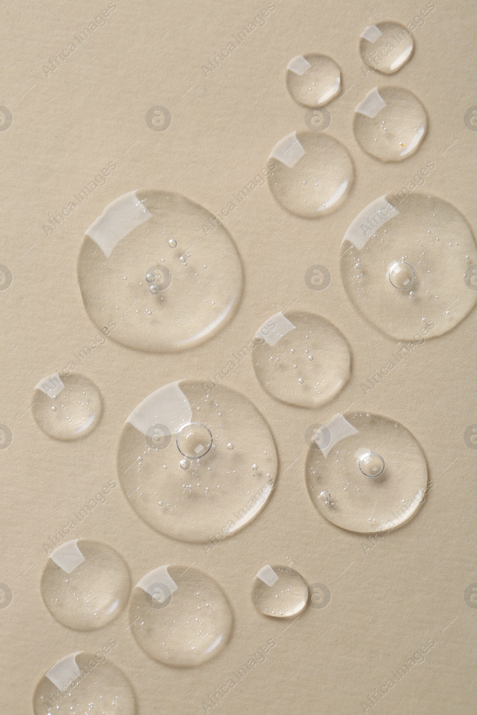 Photo of Drops of cosmetic serum on beige background, top view