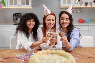 Photo of Happy young women clinking glasses of sparkling wine at birthday party in kitchen