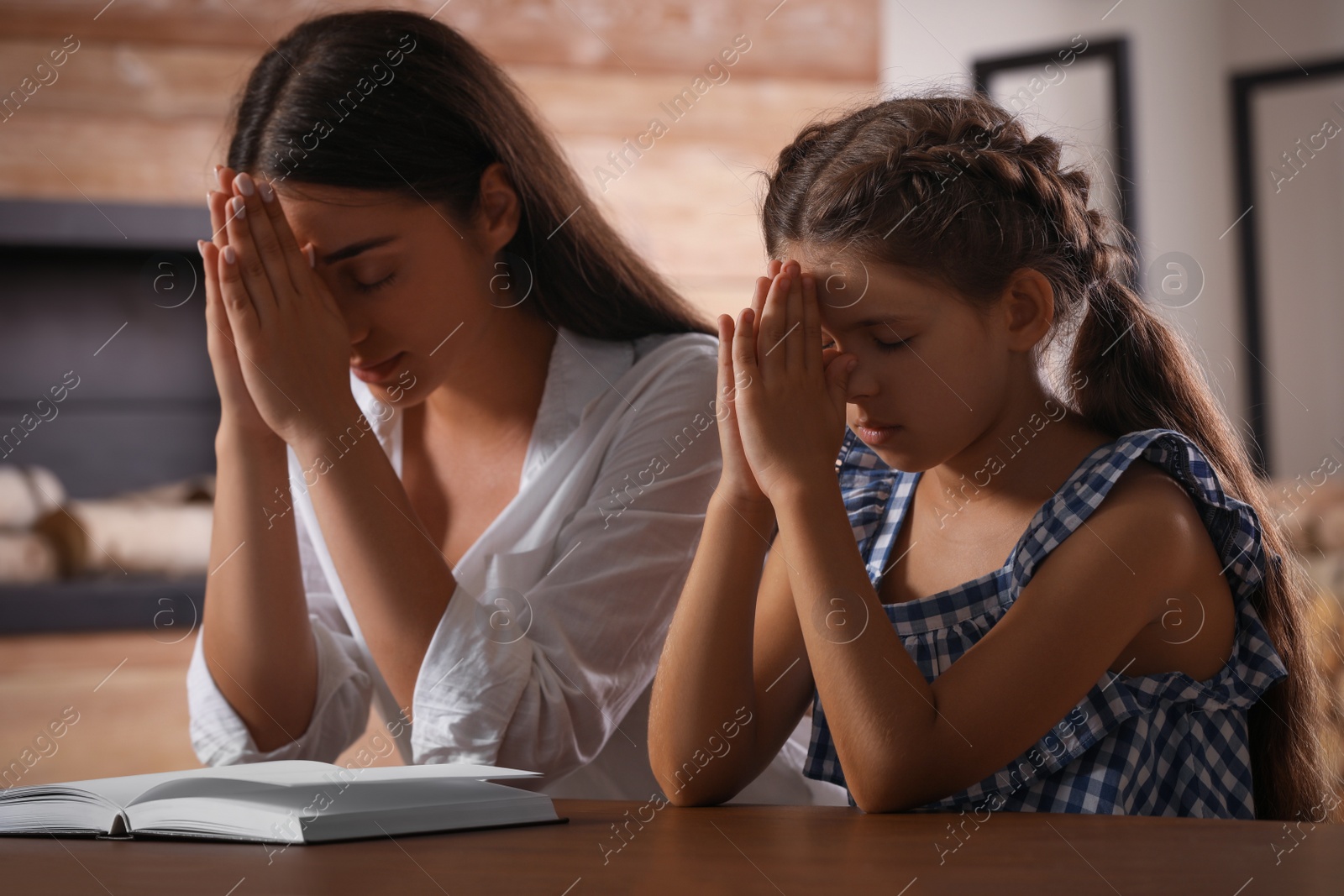 Photo of Young woman with her little daughter praying together over Bible at home