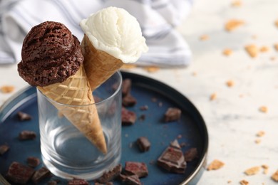 Photo of Tasty ice cream scoops in waffle cones and chocolate crumbs on light table, closeup. Space for text