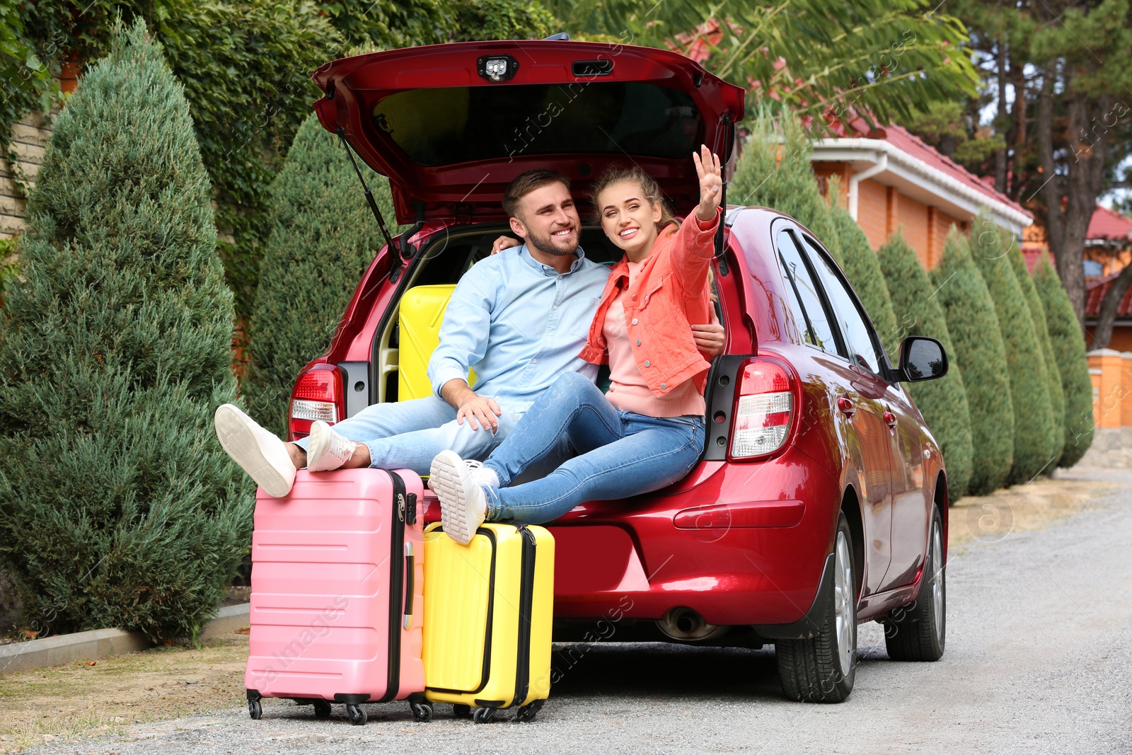 Photo of Happy young couple sitting in car trunk and suitcases outdoors