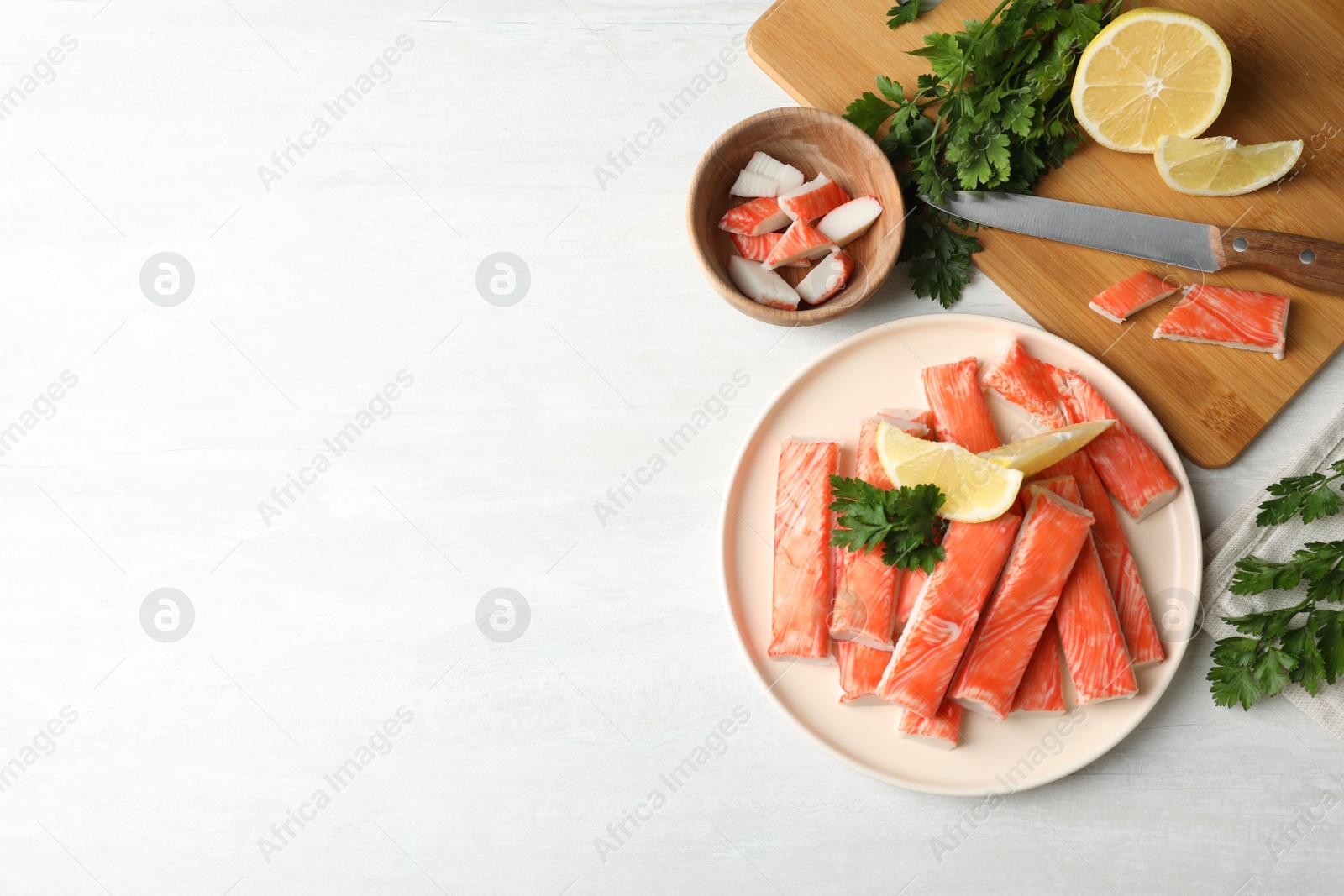 Photo of Flat lay composition with crab sticks, knife and lemon on white table, space for text