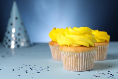 Photo of Delicious cupcakes with bright cream and confetti on blue background, closeup