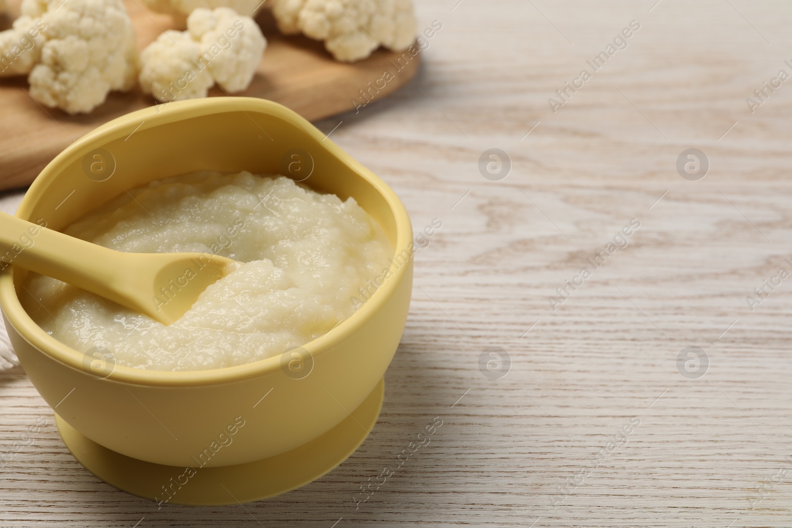Photo of Baby food. Bowl with tasty cauliflower puree on light wooden table, space for text