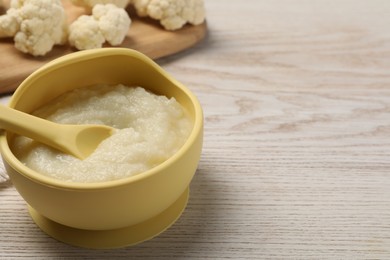 Photo of Baby food. Bowl with tasty cauliflower puree on light wooden table, space for text