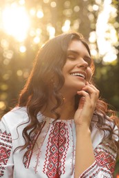Photo of Beautiful woman in embroidered shirt outdoors on sunny day. Ukrainian national clothes