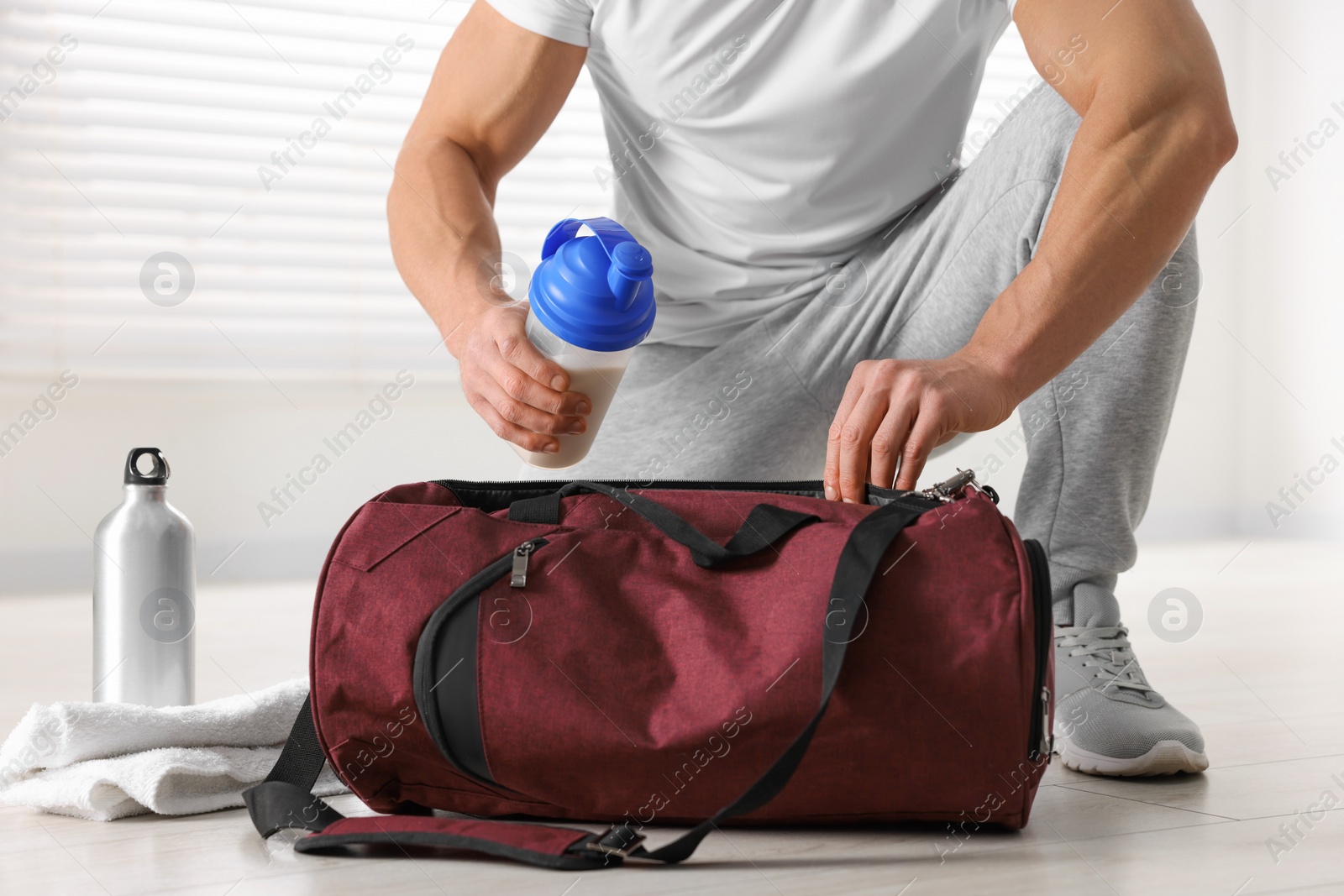 Photo of Young man putting shaker with protein into bag indoors, closeup