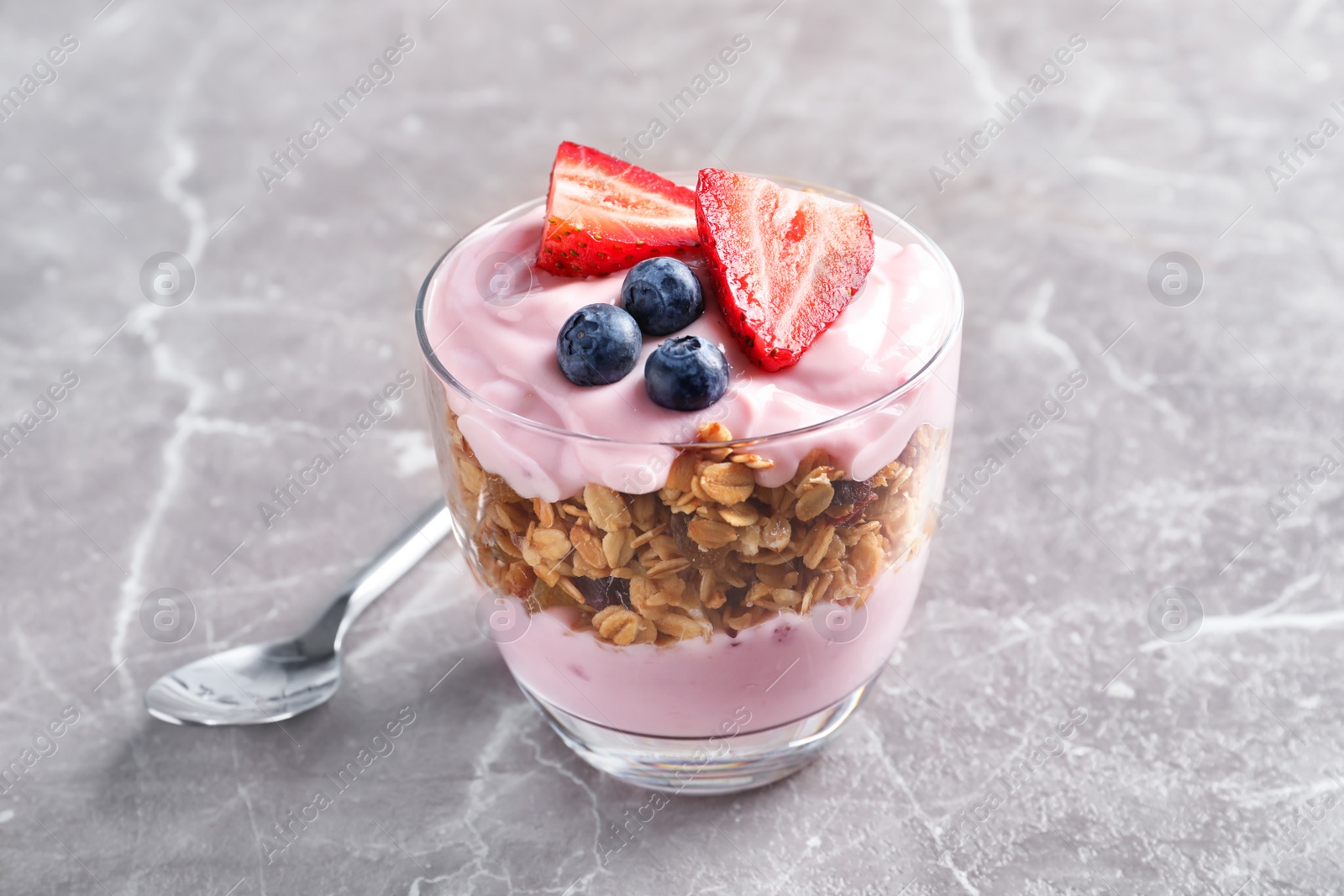 Photo of Glass with yogurt, berries and granola on table