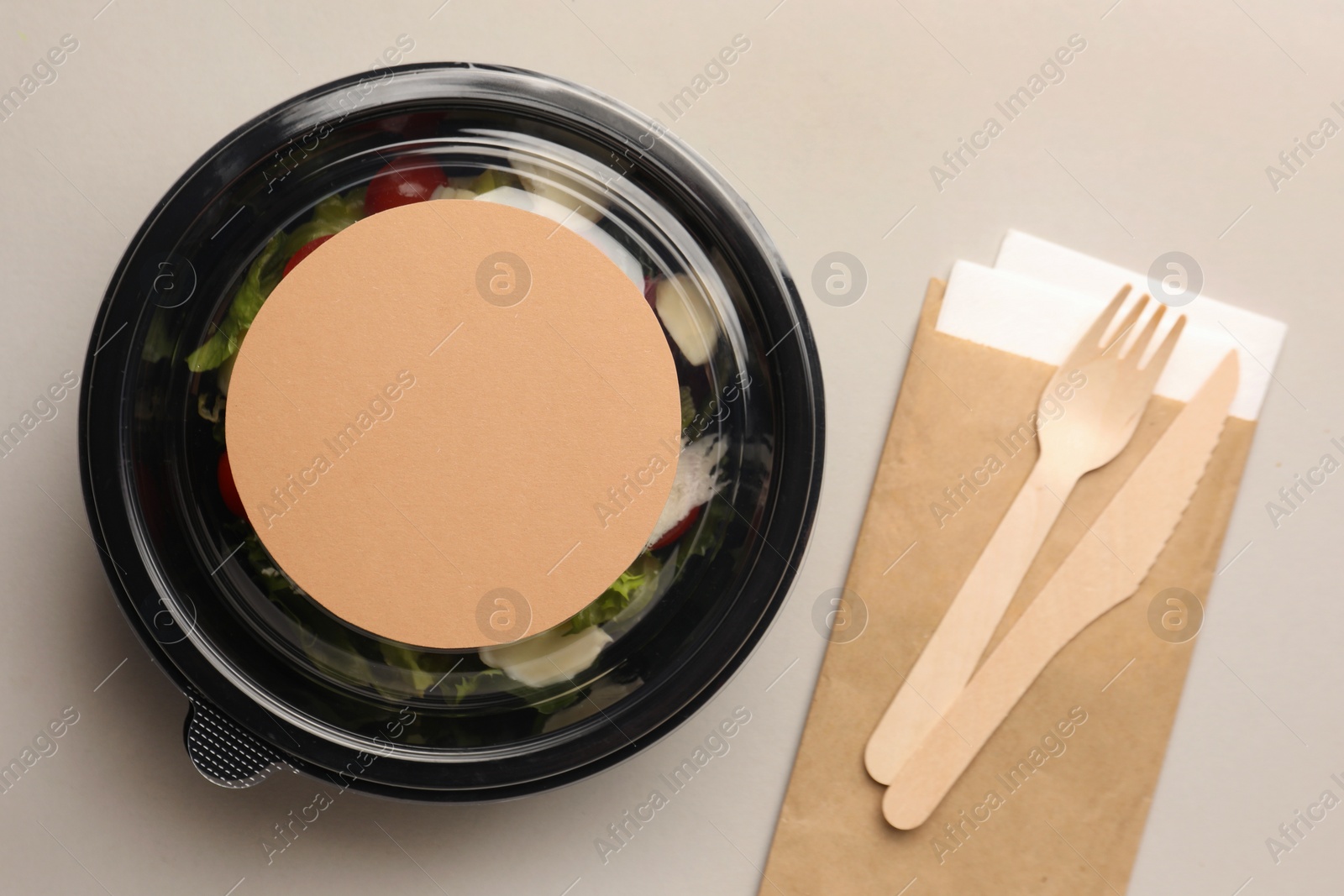 Photo of Tasty food in container with wooden fork and knife on light background, flat lay. Space for text