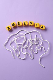 Photo of Word Amnesia and brain made of wires on violet background, flat lay