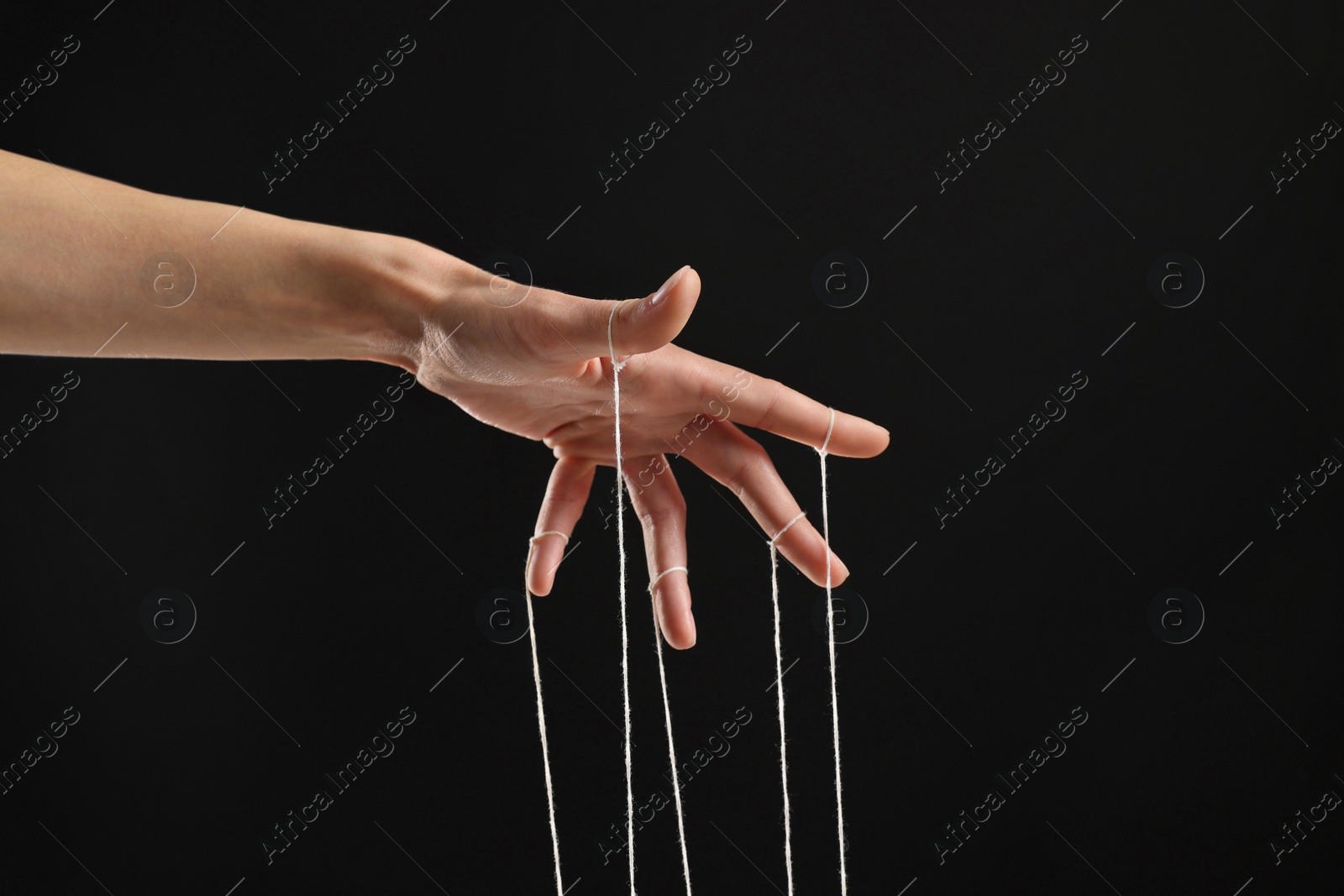 Photo of Woman pulling strings of puppet on black background, closeup