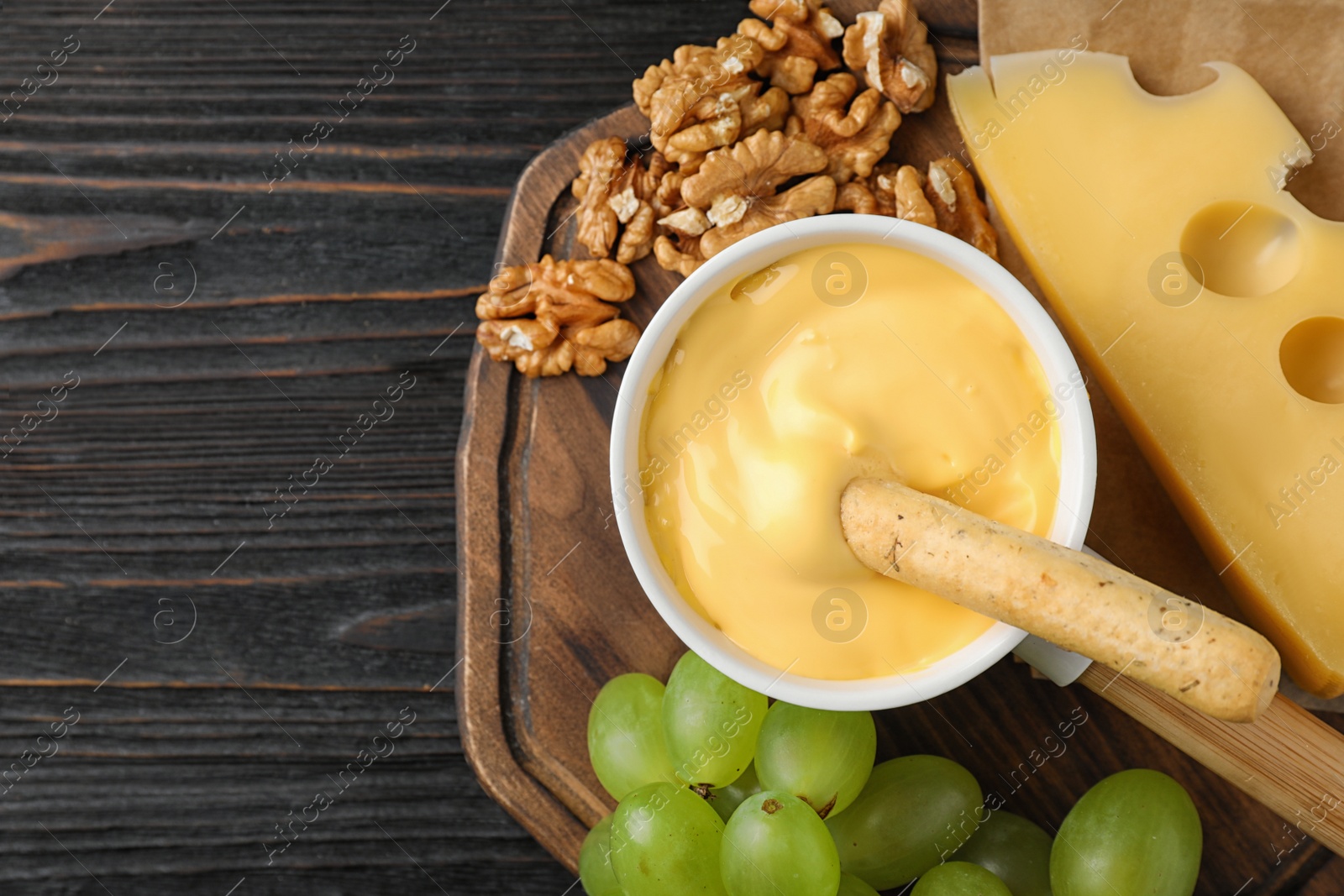 Photo of Flat lay composition with pot of tasty cheese fondue on black wooden table, space for text