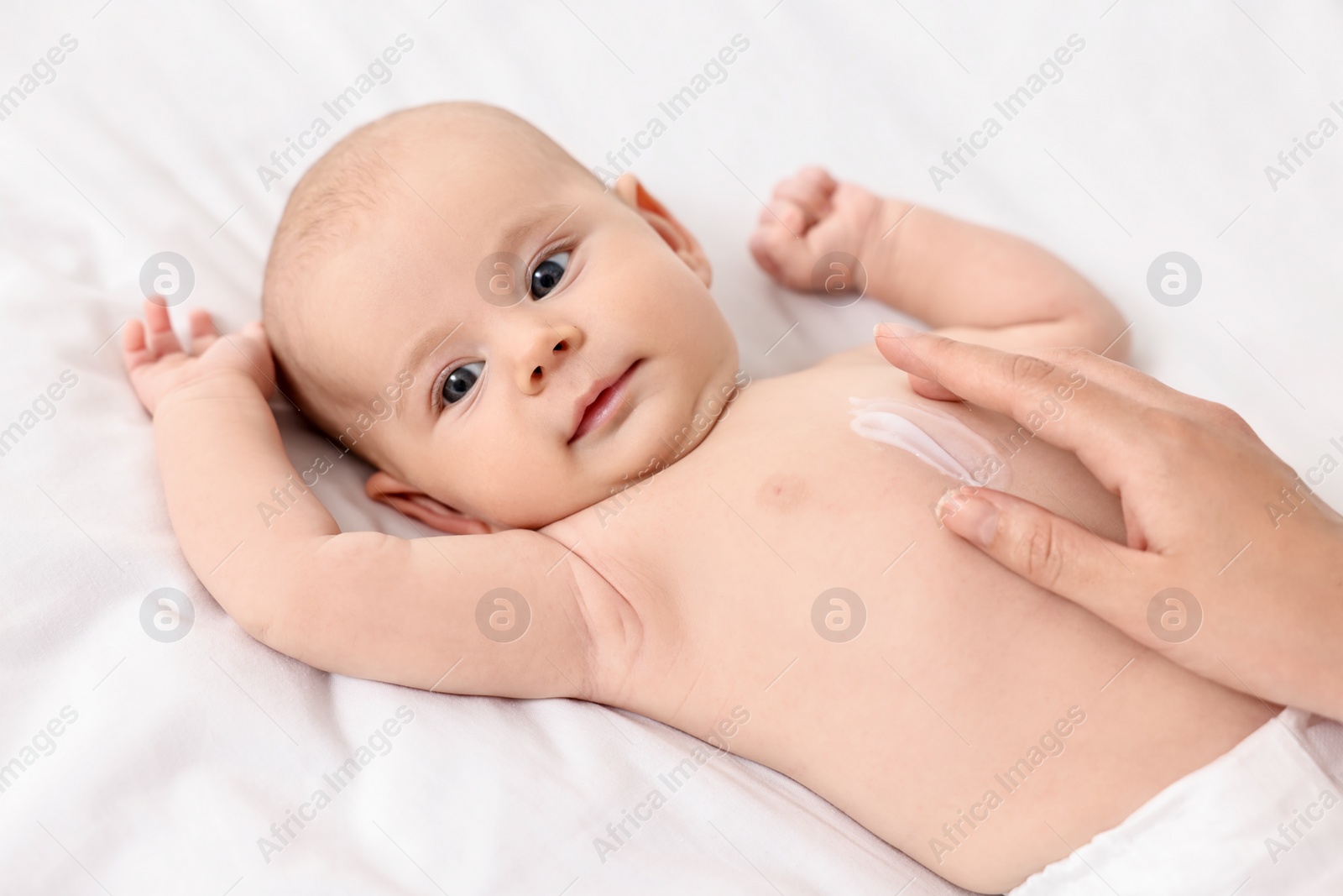 Photo of Woman applying body cream onto baby`s skin on bed, closeup