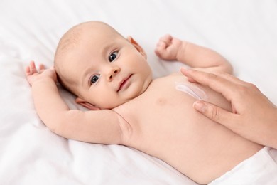 Woman applying body cream onto baby`s skin on bed, closeup