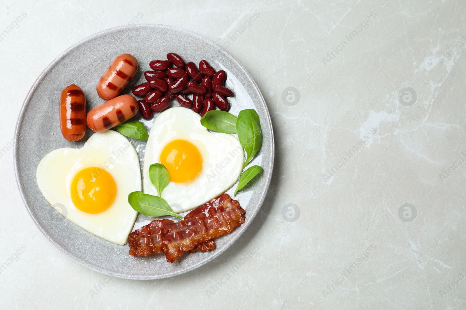 Photo of Plate of tasty breakfast with heart shaped fried eggs  on grey table, top view. Space for text