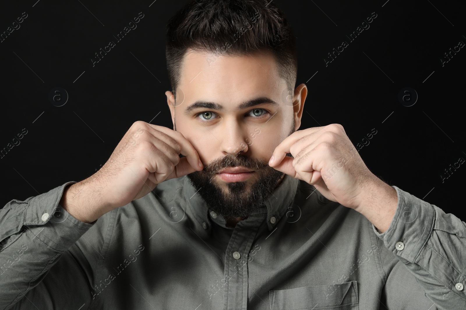 Photo of Young man in shirt touching mustache on black background