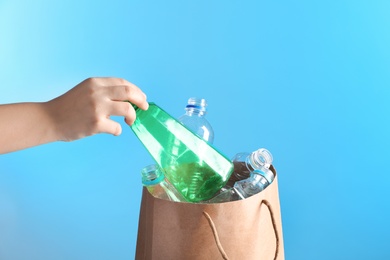 Photo of Woman putting used plastic bottle into paper bag on color background, closeup with space for text. Recycling problem