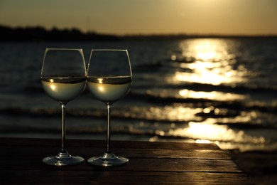 Photo of Two glasses of wine on wooden table near river at sunset. Space for text