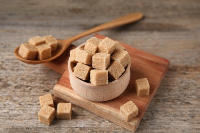 Photo of Brown sugar cubes in bowl and spoon on wooden table, closeup