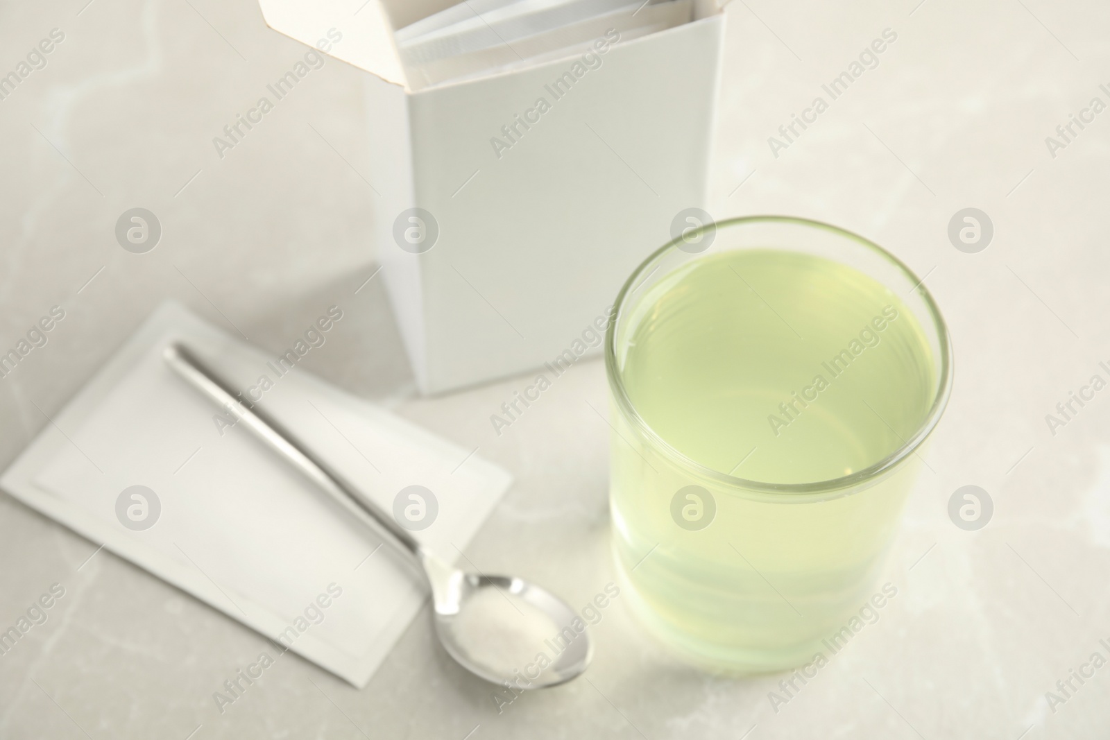 Photo of Medicine sachet, spoon and glass with dissolved drug on table indoors